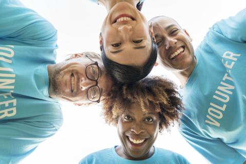 Group of happy and diverse young volunteers in a circle smiling at the camera 